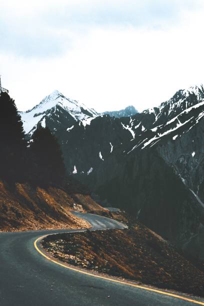 A vertical shot of a road passing trough snow-covered mounts