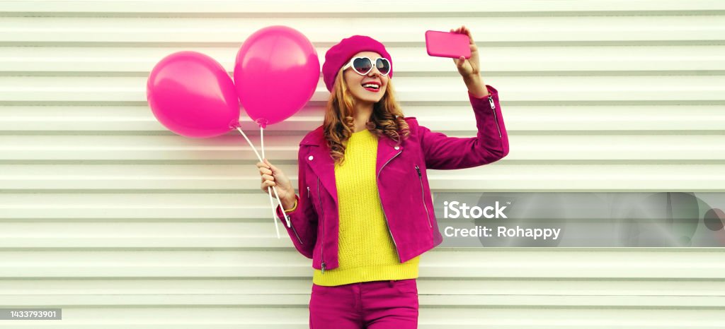 Portrait of happy smiling young woman taking selfie with phone holding pink balloons wearing beret on white background 25-29 Years Stock Photo