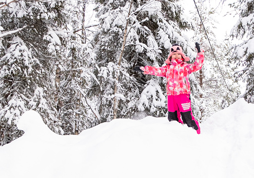 A Caucasian girl 6 years old jumps in a snowdrift in a winter forest. The child admires the beauty in nature.