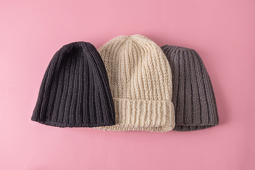Top view of wool knitted hats on soft pink background. Handmade knitted clothes, winter close concept