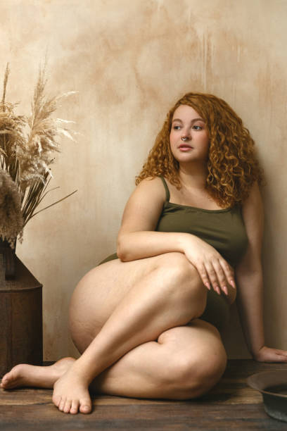 Beautiful woman in underwear Body positive model with redhead. Portrait of an attractive and voluptuous young woman posing in her lingerie against a beige background in studio plus size boho clothing stock pictures, royalty-free photos & images