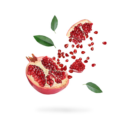 Juicy ripe pomegranate and green leaves flying on white background