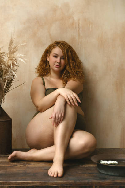 Beautiful woman in underwear Body positive model with redhead. Portrait of an attractive and voluptuous young woman posing in her lingerie against a beige background in studio plus size boho clothing stock pictures, royalty-free photos & images