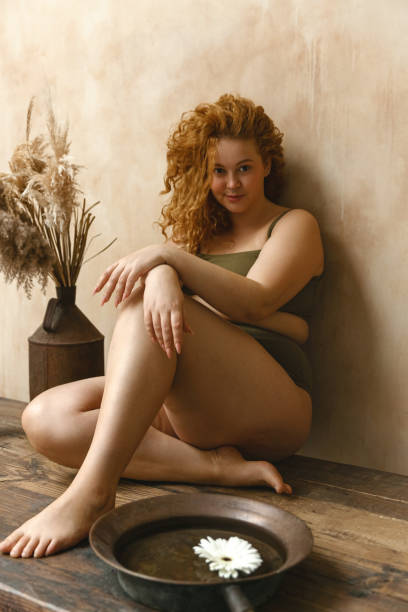 Beautiful woman in underwear Body positive model with redhead. Portrait of an attractive and voluptuous young woman posing in her lingerie against a beige background in studio plus size boho clothing stock pictures, royalty-free photos & images