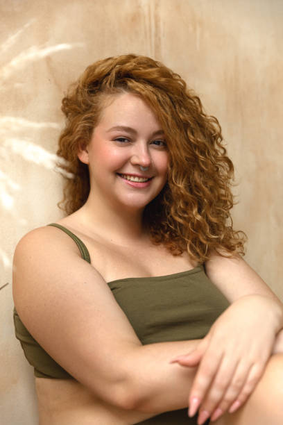 Beautiful woman in underwear Body positive model with redhead. Portrait of an attractive and voluptuous young woman posing in her lingerie against a beige background in studio plus size boho clothing stock pictures, royalty-free photos & images
