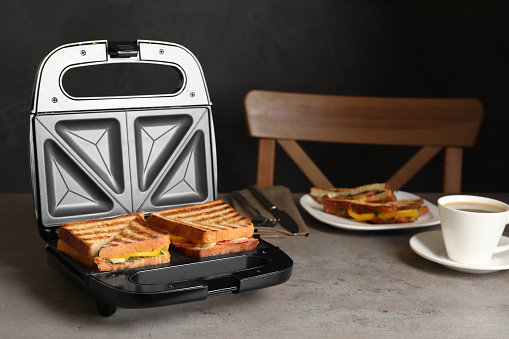 Modern grill maker with tasty sandwiches and cup of coffee on light grey table