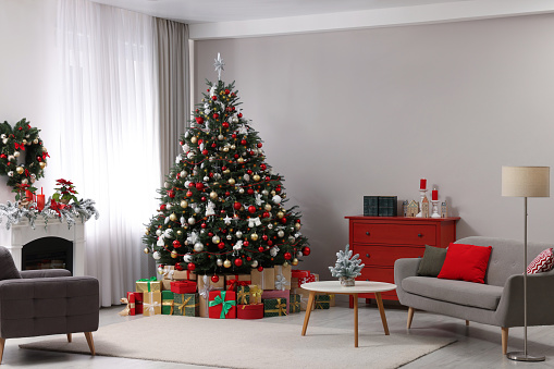 Classical Christmas decorated interior living room library with fireplace. Christmas tree with red golden ornament decorations. Modern classic style interior design apartment. Christmas eve at home
