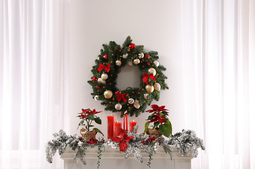Beautiful Christmas wreath on white wall over decorated mantelshelf indoors