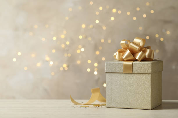 istock Beautiful golden gift box on light table against blurred festive lights, space for text 1433807215
