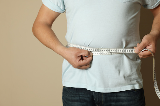 Man measuring waist with tape on beige background, closeup