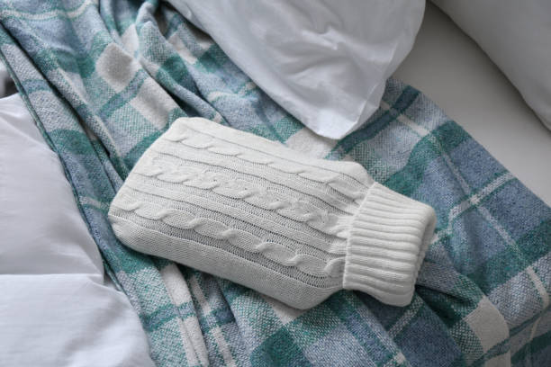 istock Hot water bottle with knitted cover and checkered plaid on bed 1433809813