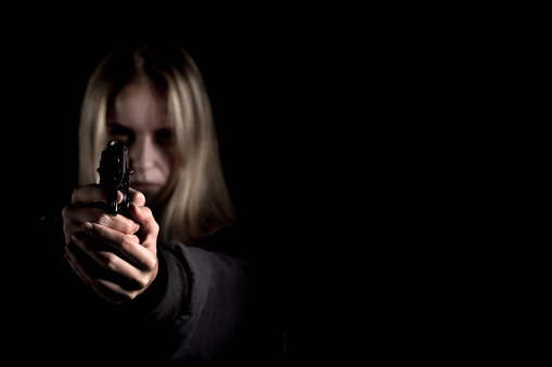 serious girl with gun aiming on black background with copyspace