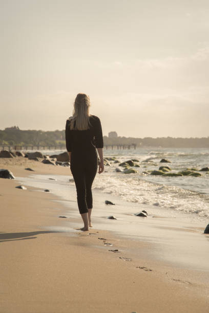woman walking away sad blond barefoot woman walking away at sunny sea beach, toned image walking beach women sadness stock pictures, royalty-free photos & images