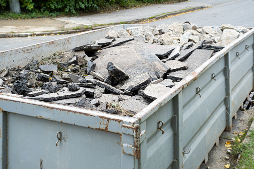 Big Overloaded dumpster waste container filled with pieces of removed asphalt, construction waste near a road digging construction site.