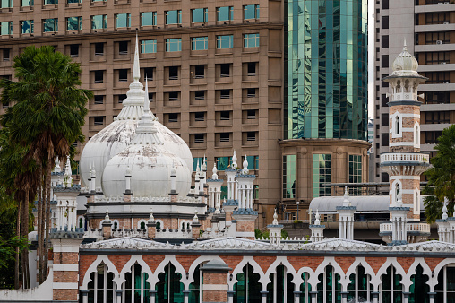 Close-up view of Masjid Jamek Mosque minarets and domes against the modern skyscrapers backgrounds, Kuala Lumpur, Malaysia.
