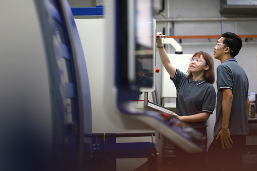 Young smiling female worker of modern industrial plant or factory in workwear and protective helmet standing in large workshop