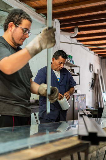 Latino men with an average age of 50 dressed casually Employees of a locksmith are working together cutting metal material