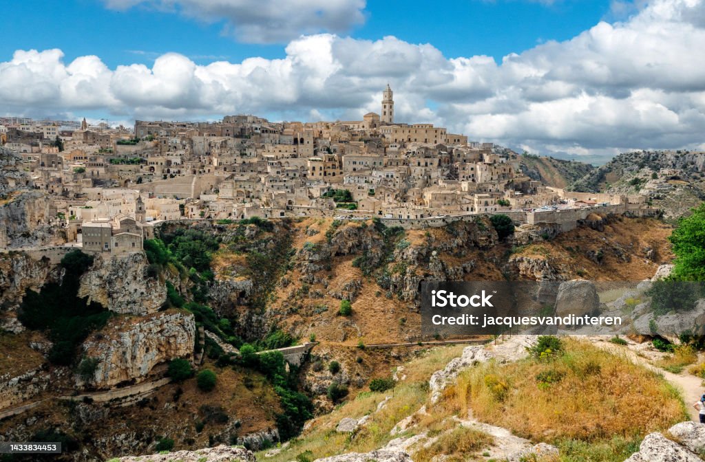 An overview of the cave city of Matera (Basilicata, Italy), located a a deep ravine (in the foreground) Matera (Basilicata, Italy) is located on a canyon, which defines Matera’s landscape and architecture. Inhabited since the Paleolithic era, established by the Romans in the 3rd century BC, the town is famous for its cave dwellings. The Sassi di Matera is the ancient town of houses carved into the rock. People lived here until the 1950s, but then they were moved because the place needed restoration. Today pubs, restaurants and hotels are found in this location. Ancient Stock Photo