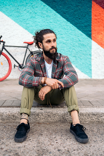 Expressive bearded man sitting in the street next to his bike against colorful background.