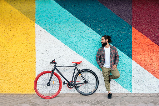 Expressive bearded man posing in the street next to his bike against colorful background.