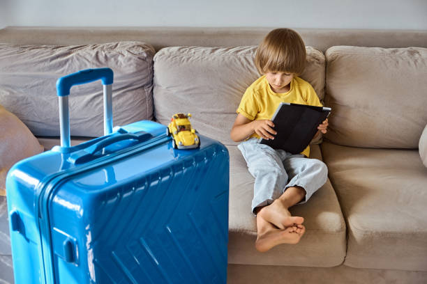 istock A sad child is sitting on a sofa using a tablet and waiting for departure. Family relocation, flight from the country 1433836904