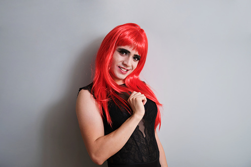 Portrait of drag queen smiling wearing a red wig on grey background. LGBTQ queer.