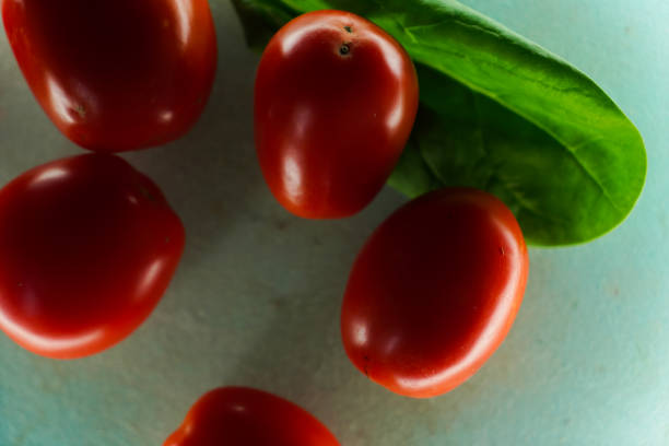Ripe sliced and whole red tomatoes on a blue background next to a spinach leaf, close-up