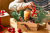 Woman's hands making christmas arrangement. Female florist creating winter ikebana with fresh pine branches, candle and christmas decorations. Small business. Seasonal winter workshop.