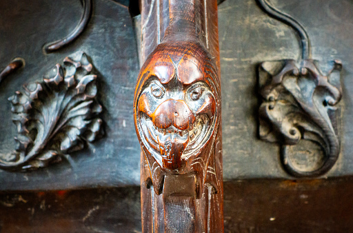 A strange carved head, possibly of an animal, on the arm of a medieval misericord stall in the chancel of the Minster church of St Margaret, King’s Lynn, in Norfolk, Eastern England, which has become shiny and paler than the surrounding wood from being handled on a regular basis. The misericords date from the 14th century.