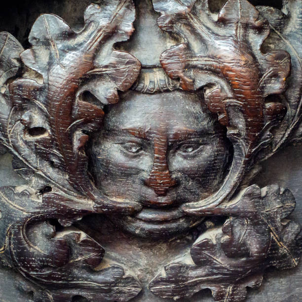 A carved head of the legendary Green Man beneath the seat of an old misericord stall in the chancel of the Minster church of St Margaret, King’s Lynn, in Norfolk, Eastern England. The misericords date from the 14th century.