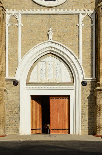 Port of Spain, Trinidad island, Trinidad and Tobago: half open wooden doors of the Catholic Cathedral Basilica of the Immaculate Conception, seat of the Archdiocese of Port of Spain - tympanum with saints, framed by plain archivolts on a red brick façade.
