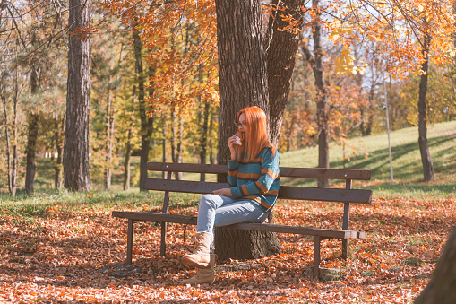 Woman eats burger in public park on sunny day in autumn