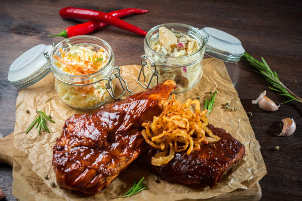 Two steaks with barbecue sauce fried onions and two glass jars of coleslaw and apple celery salad. Dish for two, served on a wooden board. stock photo