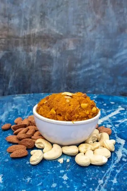 Gajar Halwa or Carrot Halwa Sweet Dessert in a White Bowl with Almond and Cashew Nut Isolated on Bluish Wooden Background in Vertical Orientation.
