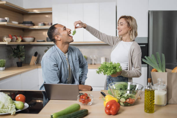 Blond young wife spouses having fun while feeding her husband with lettuce salad