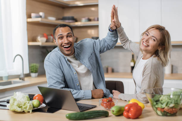 istock Attractive couple using laptop computer while preparing together healthy food giving high five 1433894370