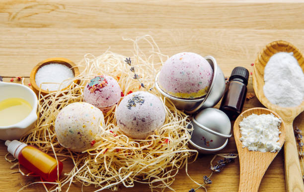 Making fizzy bath bombs at home concept. All the ingredients on table on wood spoons: cornstarch, essential oil, dye, citric acid, baking soda, dry herbs, round metal pressing molds. Copy space. stock photo
