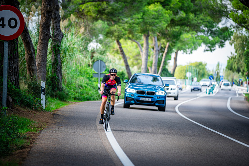 Valencia-Spain. October 13/2022. Sport cyclist riding bicycle in a country road with heavy car traffic. A speed limit sign of 40 Kilometers per hour is visible at the left.