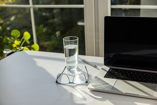 Close up of laptop, eyeglasses and drinking glass on the desk