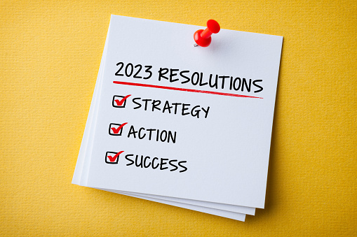 White Sticky Note With New Year 2023 Resolutions And Red Push Pin On Yellow Cardboard Background