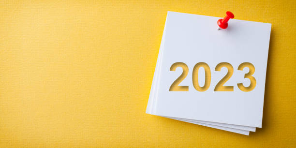 White Sticky Note With Happy New Year 2023 And Red Push Pin On Yellow Cardboard Background stock photo