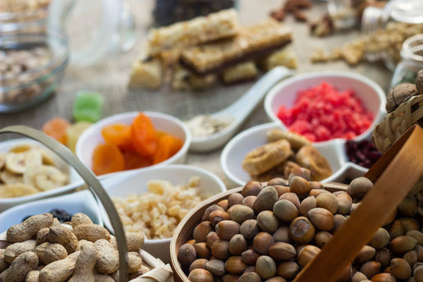 Bar with granola, dried fruits and nuts on a light wooden board with dried fruits, nuts and cereals scattered nearby