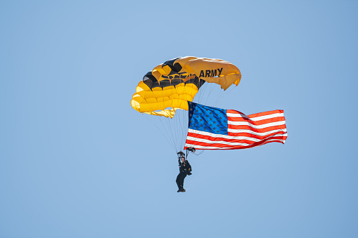 Army Paratrooper with yellow  parachute open and American flag flapping in the wind. Photo taken in non ticket area Miramar Airbase in San Diego California USA on September 23, 2022.