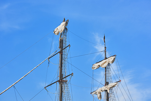 View of the masts, sails and tackle of a wooden sailboat - ropes, shrouds, rope ladders. Masts with yardarms of a wooden ship.