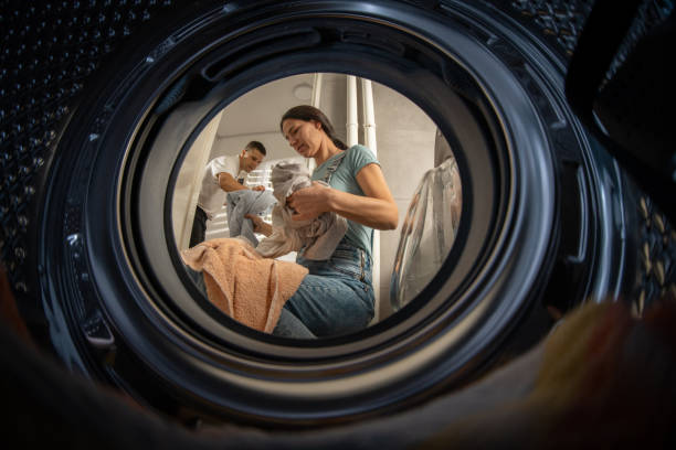 Husband and wife doing laundry Washing machine point of view, woman sitting alone in front of the washing machine in bathroom and her husband is giving her dirty laundry. laundry husband housework men stock pictures, royalty-free photos & images