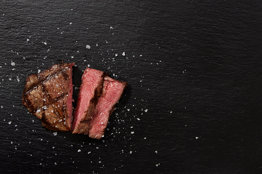 Grilled Medium Rare top sirloin beef steak or rump steak on a steel tray. Dark background. Top view.