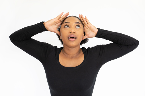 Portrait of depressed young woman holding head in hands. African American lady wearing black longsleeve looking up in stress against white background. Stress and problem concept