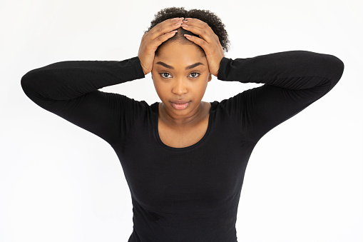 Portrait of worried young woman looking at camera. Upset African American lady wearing black longsleeve holding head in hands against white background. Stress and problem concept