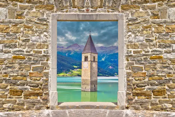 Submerged bell Tower of Curon Venosta or Graun im Vinschgau on Lake Reschen landscape view through stone wall gate, South Tyrol region Italy