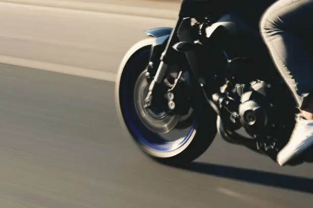 Close up shot of a front tire of a motorcycle going on the road with a motion blur.